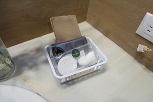 Un baño con un lavamanos blanco, un vaso de agua, una caja de pañuelos y un cable eléctrico blanco.
