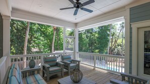 A covered porch with a ceiling fan, wooden deck, and outdoor seating area.