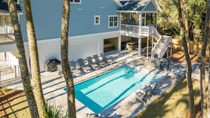 A backyard with a swimming pool, lounge chairs, a covered barbecue area, and a wooden deck.