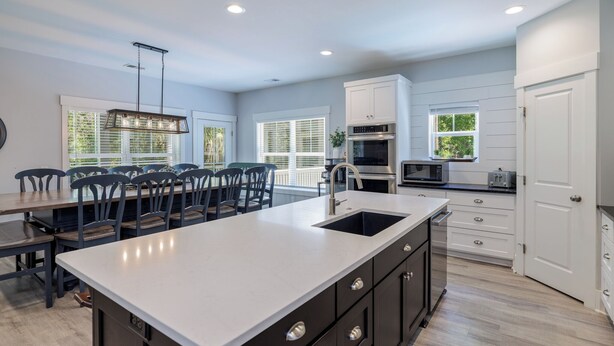 A modern kitchen with a large island, white cabinetry, and a dining area with chairs.