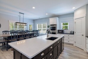 A modern kitchen with a large island, white cabinetry, and a dining area with chairs. - 6 bdrm - 5 King Suites, 6F\2H bath, 7th row, Large Pool & Outdoor area, Elevator (Hilton Head Island)