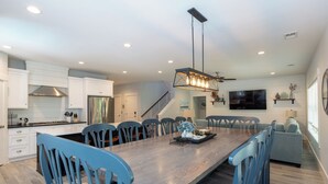 A modern kitchen with white cabinets, a stainless steel refrigerator, and a dining area with blue chairs and a wooden table.