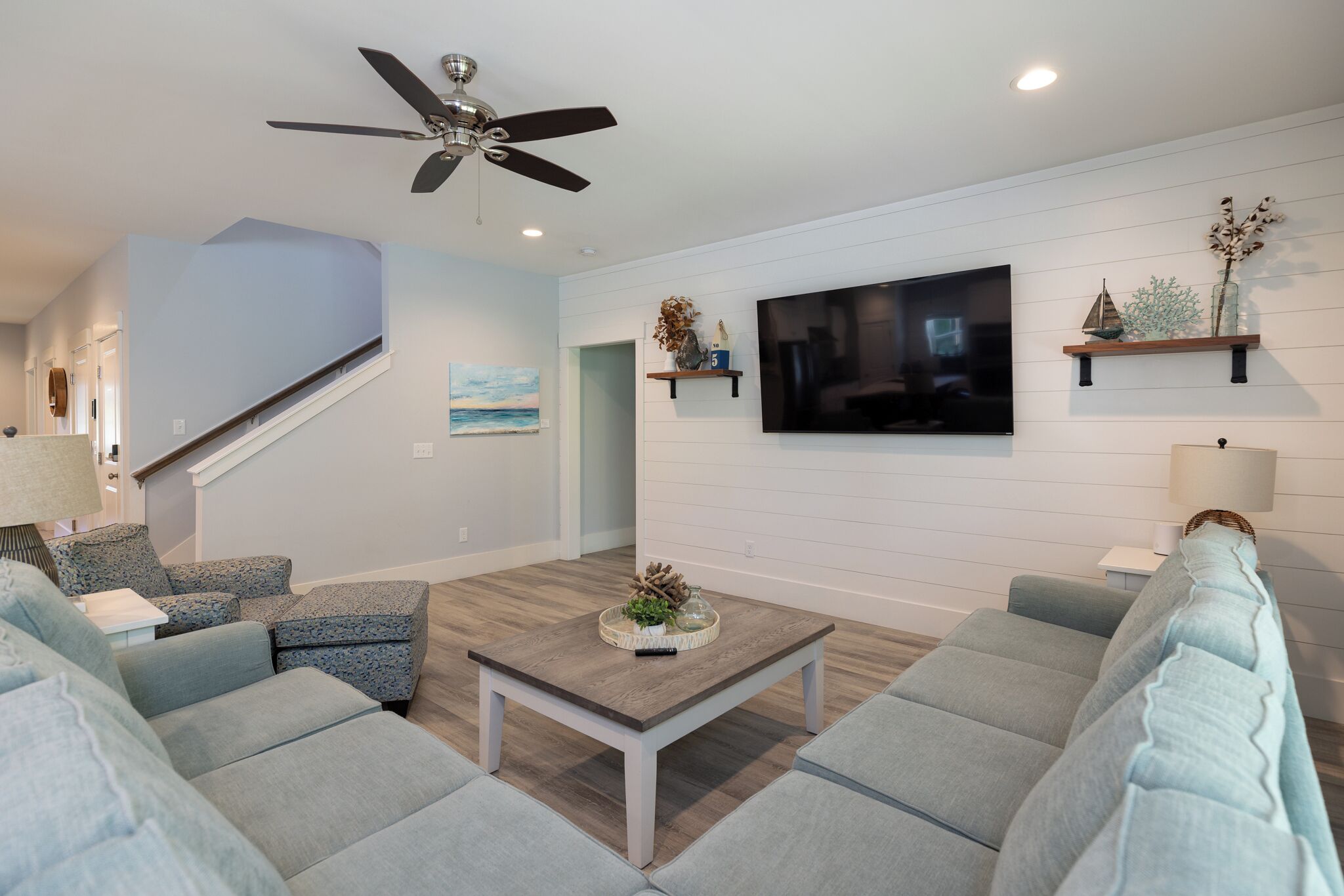 A living room with a sofa set, a coffee table, a TV, a ceiling fan, and a staircase.