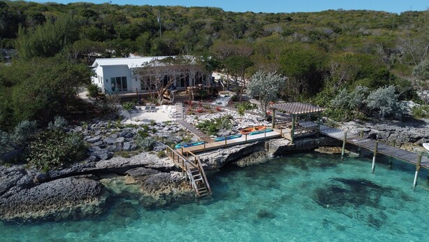 A coastal property with a white building, a wooden deck, and clear turquoise water.