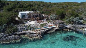 A coastal property with a white building, a wooden deck, and clear turquoise water. - Waterfront Retreat with POOL & DOCK on Hoopers Bay (Georgetown)
