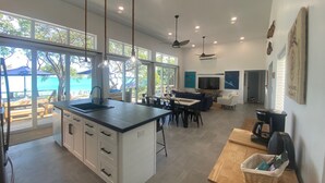 A modern kitchen with a large island, dining area with a TV, and a view of the ocean.