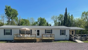 A single-story mobile home with a front deck, two outdoor seating areas, and a covered patio.