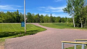 A gravel path leading to a wooden deck with a mailbox and a signpost in a park.
