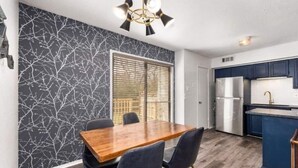 Una cocina moderna con armarios oscuros, un refrigerador de acero inoxidable y una mesa de comedor de madera con sillas.
