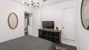 Un dormitorio con cama, televisión sobre un mueble, espejo y una puerta.
