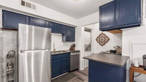 Cocina compacta con gabinetes azul oscuro, un refrigerador de acero inoxidable y una pequeña isla con encimera.