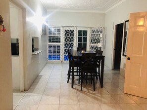 A dining area with a table and chairs, a kitchen area with a refrigerator, and a door leading to another room.