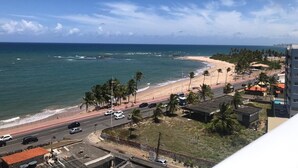 Blick auf die Küste mit Strand, Palmen und einer Straße, die zu einem Gebäude führt.