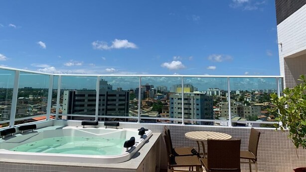 Eine Dachterrasse mit Whirlpool, Sitzgelegenheit und weiter Aussicht auf die Stadt.