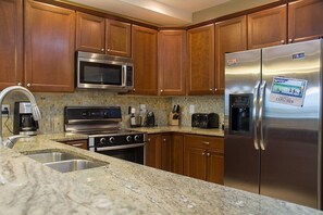 A kitchen with wooden cabinets, stainless steel appliances including a refrigerator, microwave, and oven, and a granite countertop.