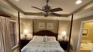 A four-poster bed with a ceiling fan, two bedside lamps, and a bathroom visible through an open door.