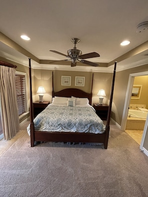 A four-poster bed with a ceiling fan, two bedside lamps, and a bathroom visible through an open door.