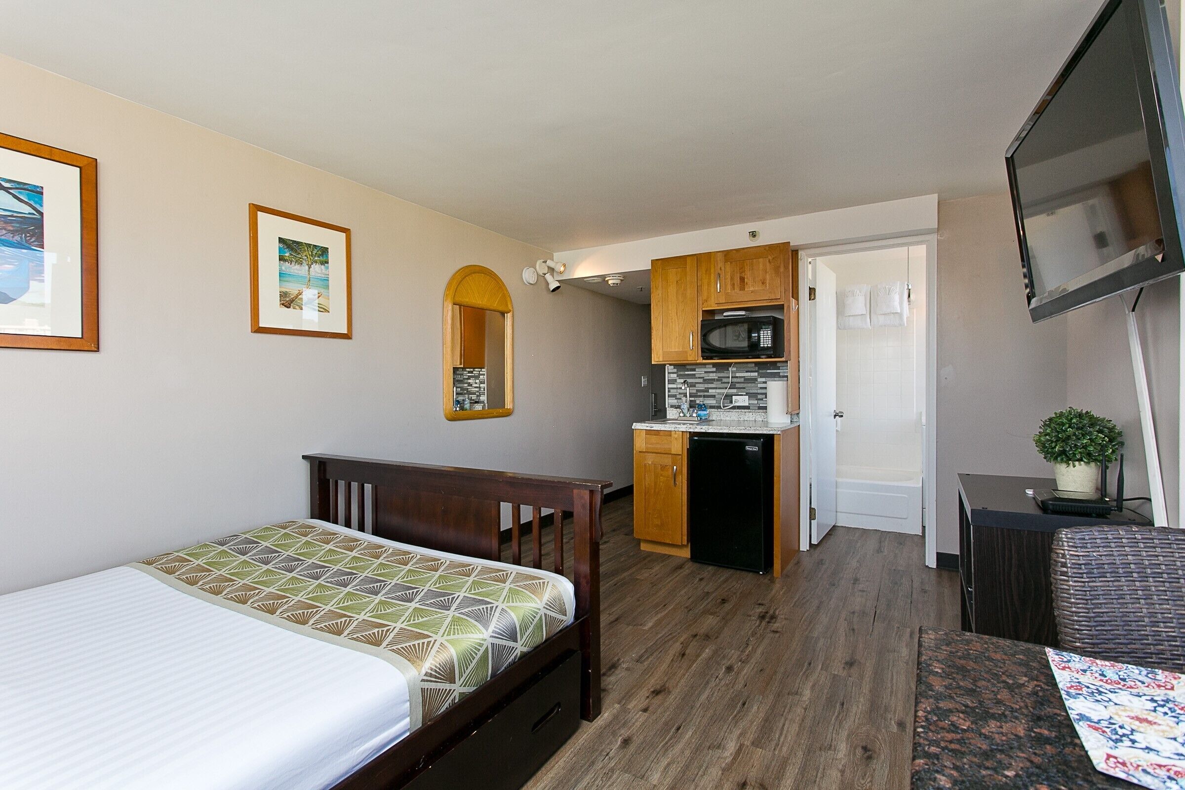 Una habitación compacta con cama, una kitchenette pequeña, un televisor y una puerta que conduce a otra habitación.
