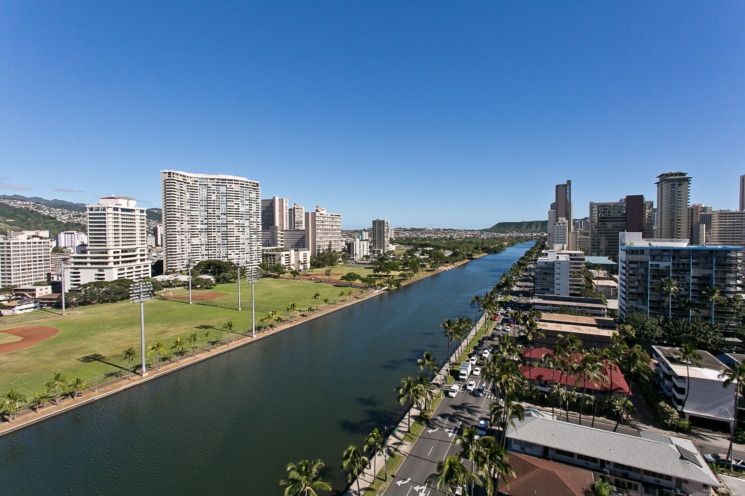 A river running through a city with modern buildings and a sports field on one side.