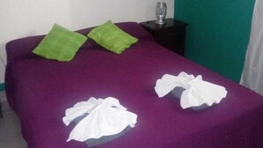 A bed with a purple bedspread, two green pillows, and two white towels. - Bambi (La Falda)