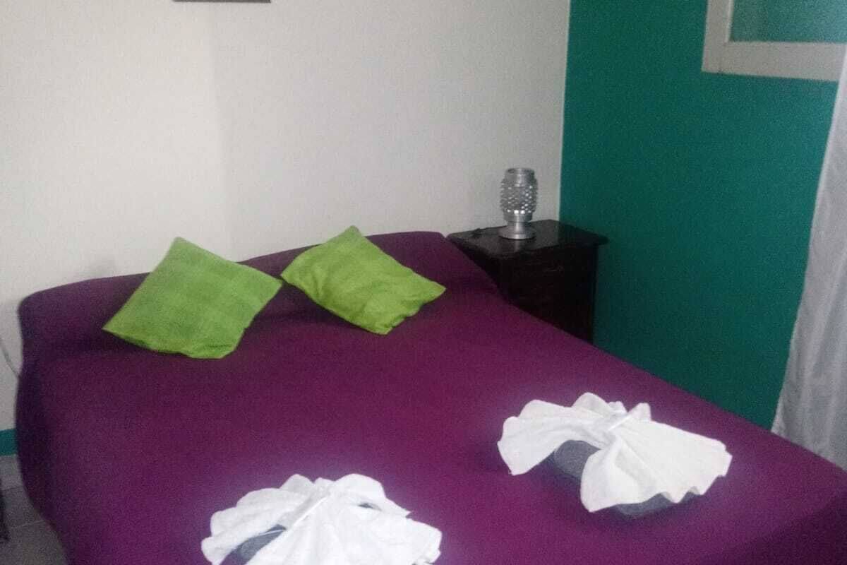 A bed with a purple bedspread, two green pillows, and two white towels.