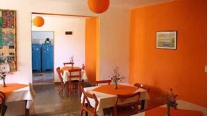 A dining area with orange walls, white tables, and chairs. There is a door leading to another room. - Bambi (La Falda)