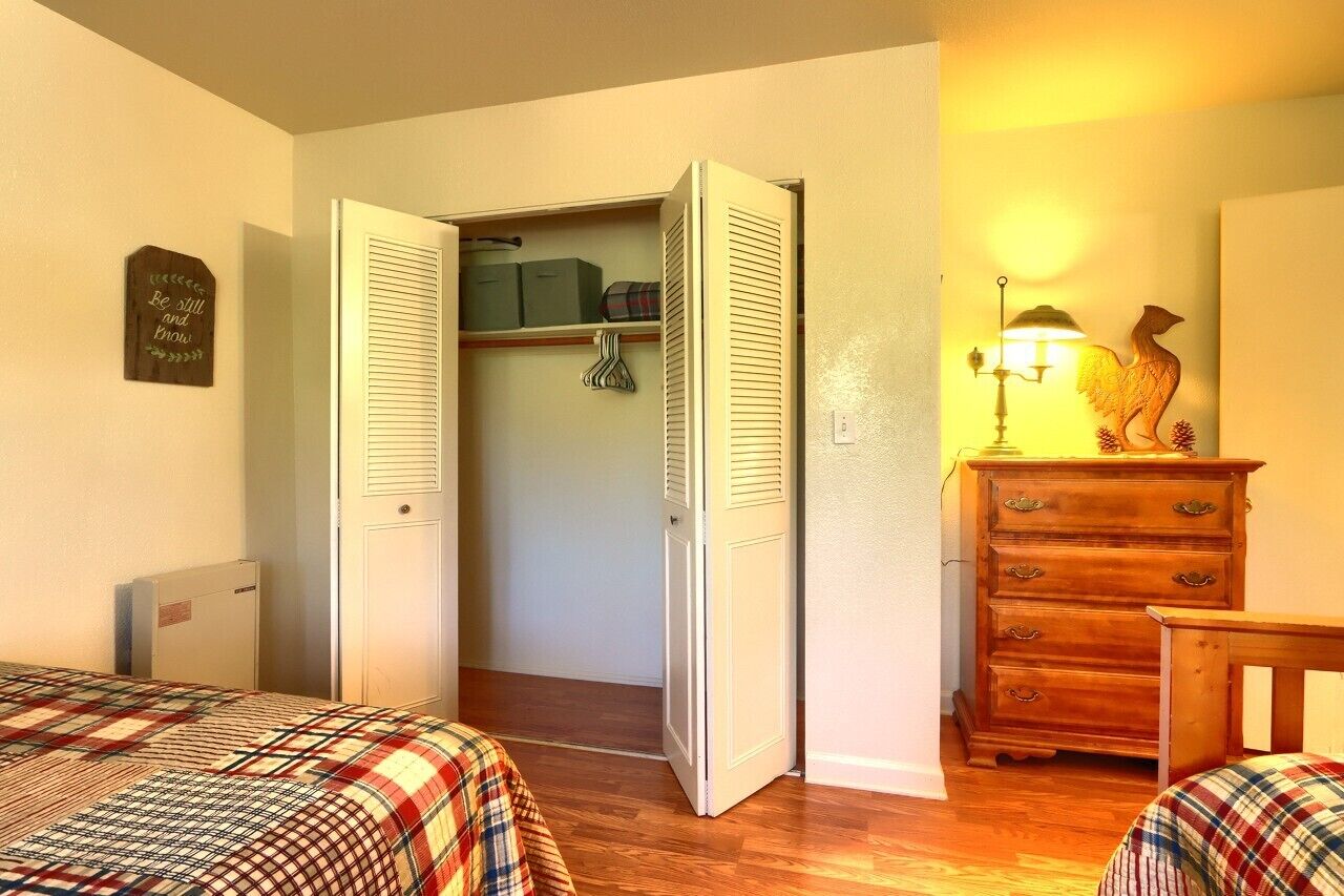 A bedroom with a bed, a dresser, a lamp, and a closet with a sign.