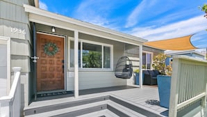 A house with a wooden front door, a porch with steps, and a hanging chair. - Felspar House · Clean, Charming House in PB 🏖☀️ AC, pkg & laundry (San Diego)