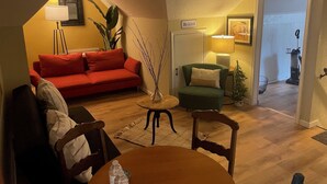 A cozy living room with a red sofa, a green armchair, a small round table, and a lamp. - Quaint Studio Space, right next to Macalester College, 5 miles uptown/downtown (Saint Paul)