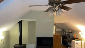 A cozy living room with a wood-burning stove, a television, and a ceiling fan. - Quaint Studio Space, right next to Macalester College, 5 miles uptown/downtown (Saint Paul)