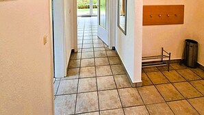 A hallway with tiled flooring, a door leading to a balcony, and a trash bin.