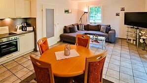 A compact living space with a dining area, kitchenette, sofa, and TV.