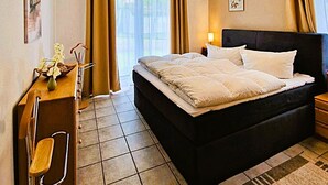 A hotel room with a bed, a desk, a chair, a lamp, and a window with curtains.