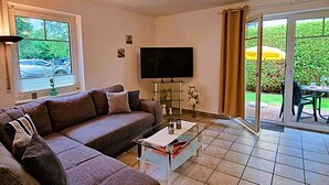 A living room with a sofa, a coffee table, a flat-screen TV, and a sliding glass door leading to an outdoor area.