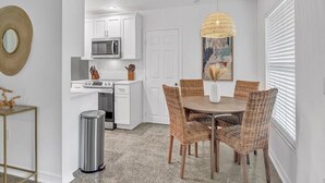 A modern kitchen with white cabinets, a microwave, and a dining area with wicker chairs and a round table. - 3-bedroom-2 Full Baths Beach House mnts to Central Beach & downtown (Vero Beach)