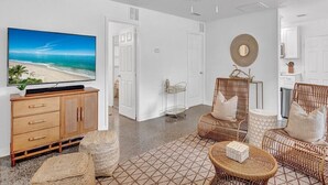 A living room with a television, wicker furniture, a ceiling fan, and a kitchen area in the background. - 3-bedroom-2 Full Baths Beach House mnts to Central Beach & downtown (Vero Beach)