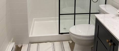Een badkamer met een douchecabine van glas, een wit toilet en een klein raam.