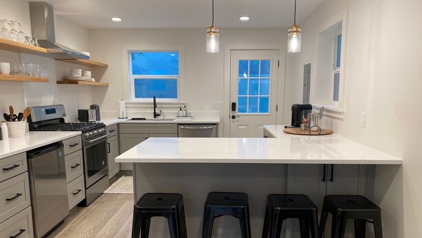 A modern kitchen with a central island, bar stools, stainless steel appliances, and pendant lighting. - Remodeled Studio Cottage! Walk to Lake and Hiking Trails (Fall City)