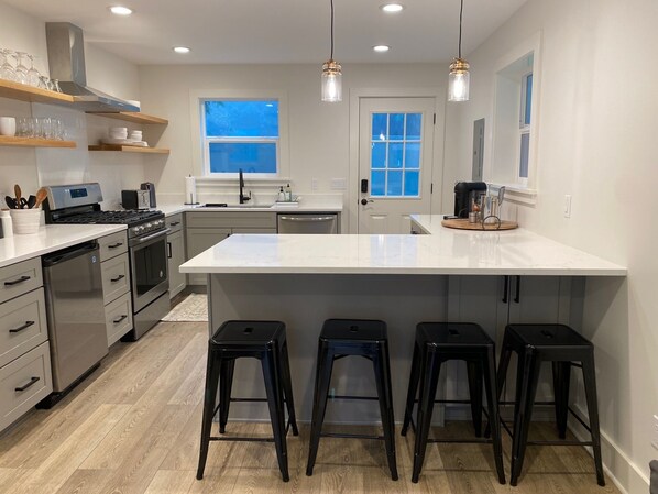 A modern kitchen with a central island, bar stools, stainless steel appliances, and pendant lighting.