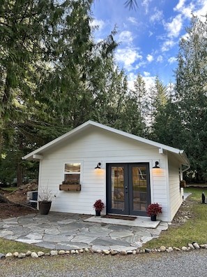 A small, single-story cabin with a stone-paved entrance, surrounded by dense forest.