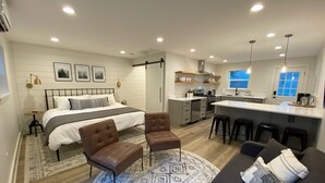 A modern bedroom with a large bed, a sitting area with a sofa and chairs, a kitchen with a bar, and a dining area. - Remodeled Studio Cottage! Walk to Lake and Hiking Trails (Fall City)