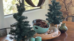 Ein Holztisch mit einer kleinen Weihnachtstanne, einer Schale Tannenzapfen und einem dekorativen Rentier.