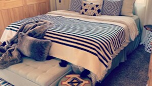Ein Schlafzimmer mit einem Bett, Kissen, einer Decke, einer Bank und einem kleinen Hocker.
