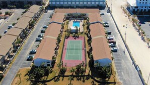 Un grande hotel con campo da tennis, parcheggio e vista sulla spiaggia.