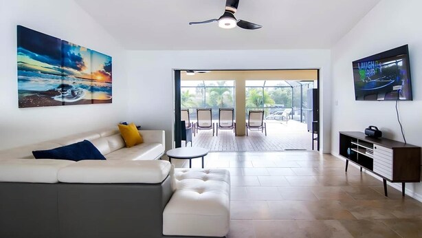 A modern living room with a sofa, a coffee table, and a TV. There is a balcony with chairs and a table.