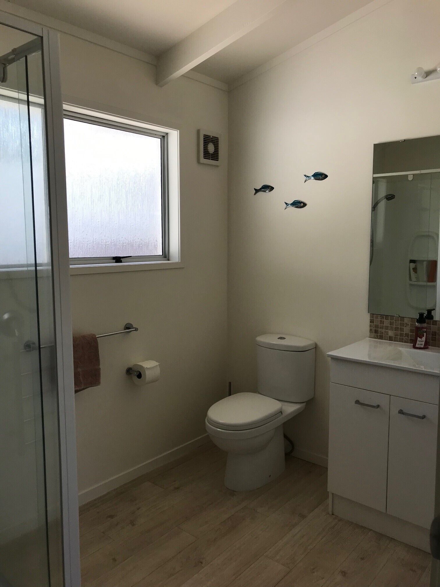 A small bathroom with a toilet, a sink, a mirror, and a window.
