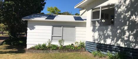 Ett enplanshus med ett sluttande tak, ett litet garage som är sammanbyggt med huset och en framträdgård med gräsmatta och ett blomsterland.