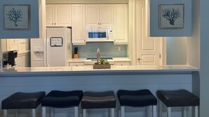 A modern kitchen with white cabinets, a built-in microwave, a water dispenser, and a bar area with stools. - RELAX and Save! Escape on sunny Fort Myers Beach in a 2BR/2BA w/ Pool/ Gulf view (Fort Myers Beach)