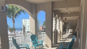 A balcony with turquoise chairs, a view of the ocean, and a building in the background. - RELAX and Save! Escape on sunny Fort Myers Beach in a 2BR/2BA w/ Pool/ Gulf view (Fort Myers Beach)