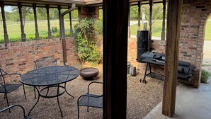Una veranda esterna con parete in mattoni, un tavolo rotondo e sedie in metallo.